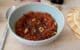 Une assiette creuse contenant une crème de poivrons rôtis avec des éclats de noix et de l'huile d'olive