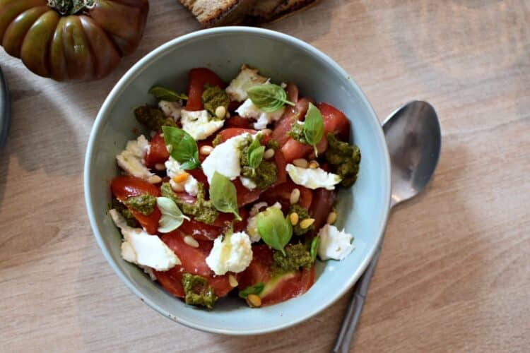 Une assiette creuse contenant des tomates coupées avec de la mozarella et du pesto