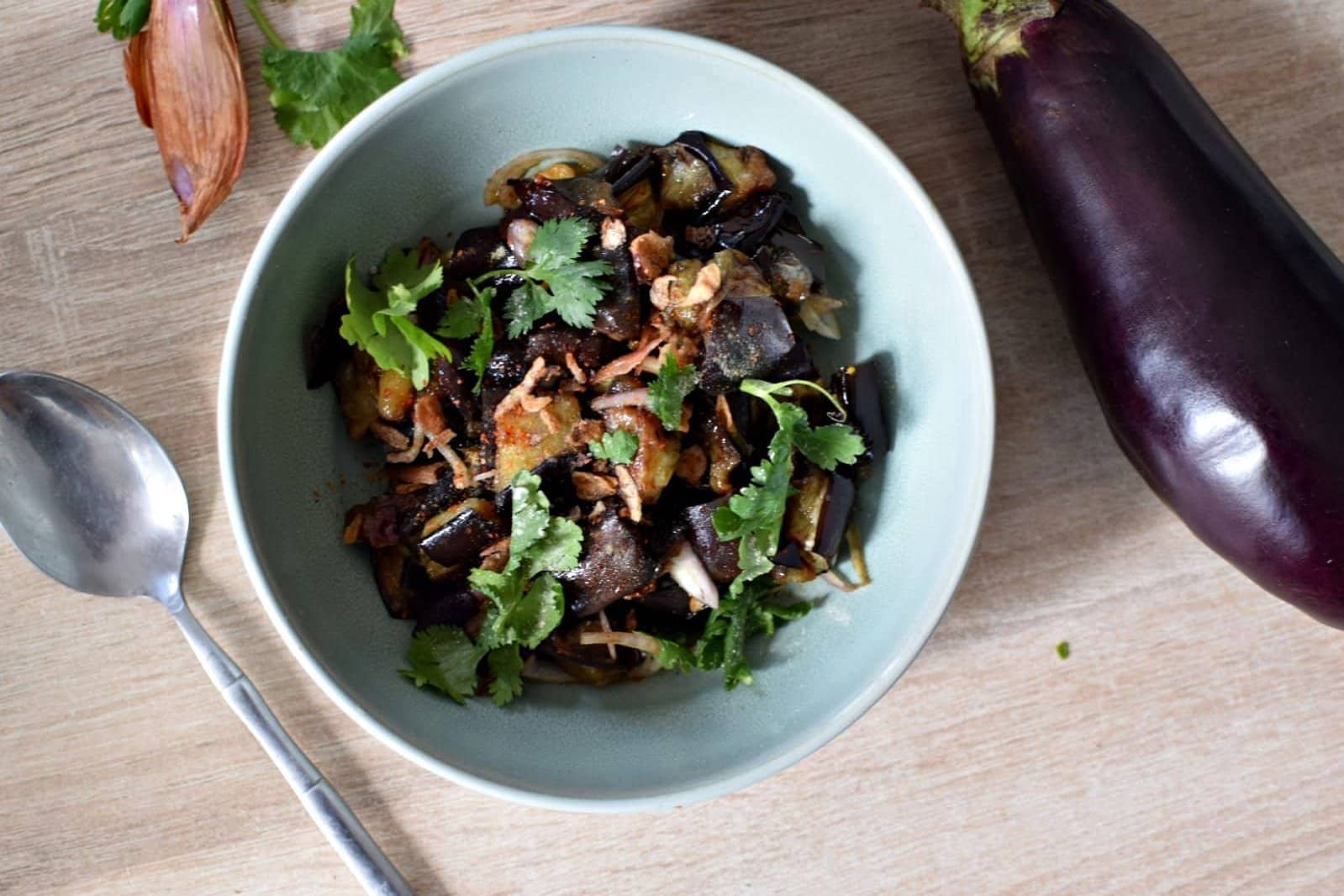 Une vue du dessus d'une assiette creuse contenant des aubergines marinées à la thaïlandaise avec des herbes fraîches