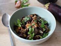 Une assiette creuse bleue, avec des aubergines confites en salade et de la coriandre fraîche sur le dessus