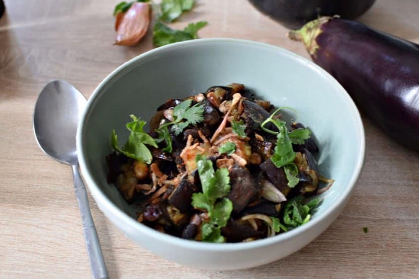 Une assiette creuse bleue, avec des aubergines confites en salade et de la coriandre fraîche sur le dessus