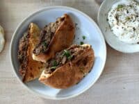une assiette contenant des pains libanais farcis avec de la viande, des épices et des herbes, à côté une petite coupelle remplie de sauce blanche