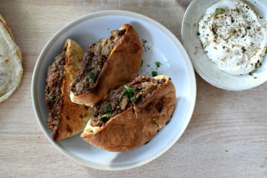 une assiette contenant des pains libanais farcis avec de la viande, des épices et des herbes, à côté une petite coupelle remplie de sauce blanche