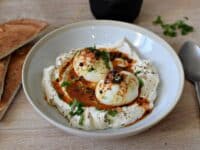 une assiette creuse, avec un lit de yaourt crémeux, et des oeufs mollets avec une sauce au beurre épicé