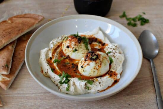 une assiette creuse, avec un lit de yaourt crémeux, et des oeufs mollets avec une sauce au beurre épicé